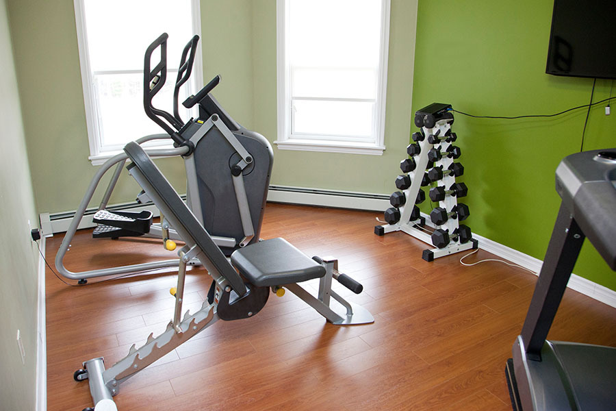 A small workout room inside an apartment or house with bench, weights and elliptical